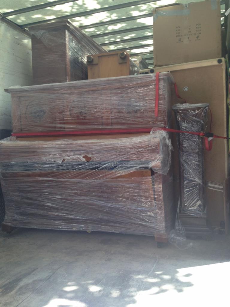 Mebel oklejony folią stretch i zabezpieczony pasami wewnątrz pojazdu dostawczego. Widoczne kartony i inne przedmioty. Przygotowanie do transportu.