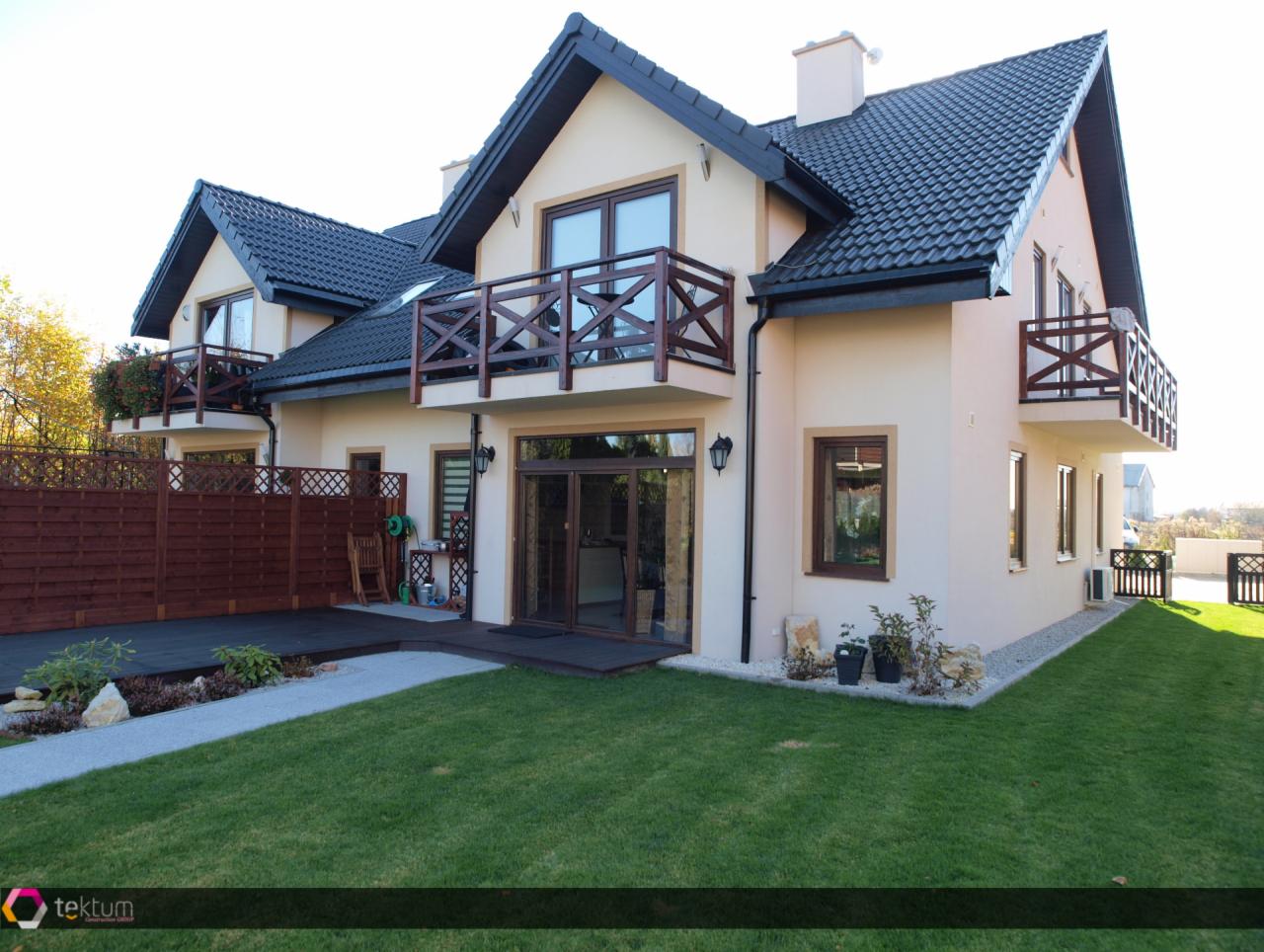 Gotowy dom bliźniak w technologii szkieletowej z ciemną dachówką i drewnianymi balkonami, widok z trawnika.