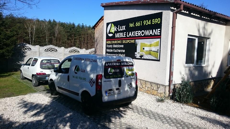 Budynek lakierni meblowej Lak-Lux z reklamą na ścianie, firmowym autem dostawczym i osobowym na podjeździe. Reklama informuje o meblach lakierowanych.