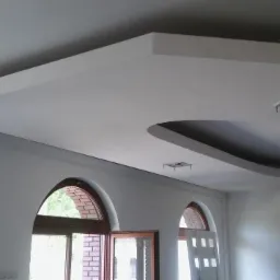 Sufit podwieszany z dekoracyjnym, łukowym obniżeniem i oświetleniem punktowym, widoczne dwa łukowe okna w tle.