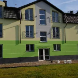 Dwukolorowa elewacja budynku wielorodzinnego z balkonami, świeżo po malowaniu, z widocznymi pustakami na trawniku przed budynkiem.