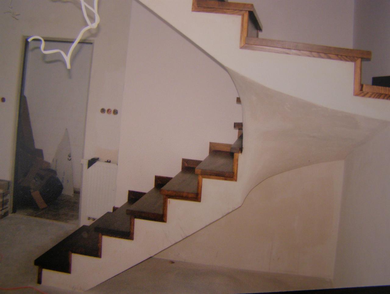 Nowoczesne schody drewniane ze ścianą o zaokrąglonym kształcie, widoczne z boku, z surowym wykończeniem wnętrza w tle. Elementy drewniane w ciemnym odcieniu brązu.