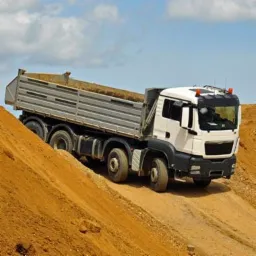 Wyładowany wywrotką materiał sypki na nierównym terenie, błękitne niebo w tle. Widok z dołu, ekspozycja na pojazd i nasyp.