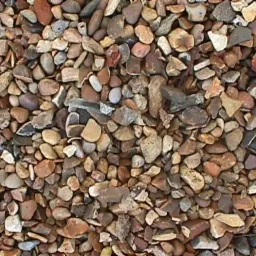 Drobny, brązowo-szary żwir rzeczny o nieregularnych kształtach, wypełniający całą powierzchnię kadru. Widoczne pojedyncze, większe kamienie.