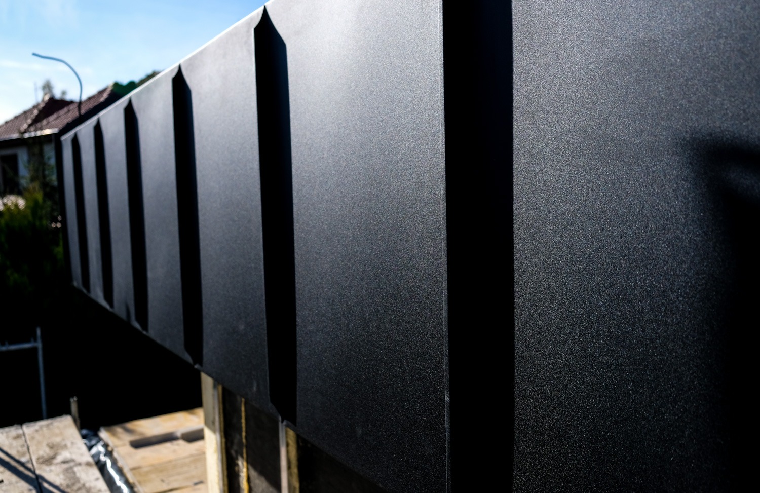 Nowoczesne, grafitowe obróbki blacharskie na dachu domu jednorodzinnego, widoczne z dołu pod kątem, z elementami rusztowania w tle.