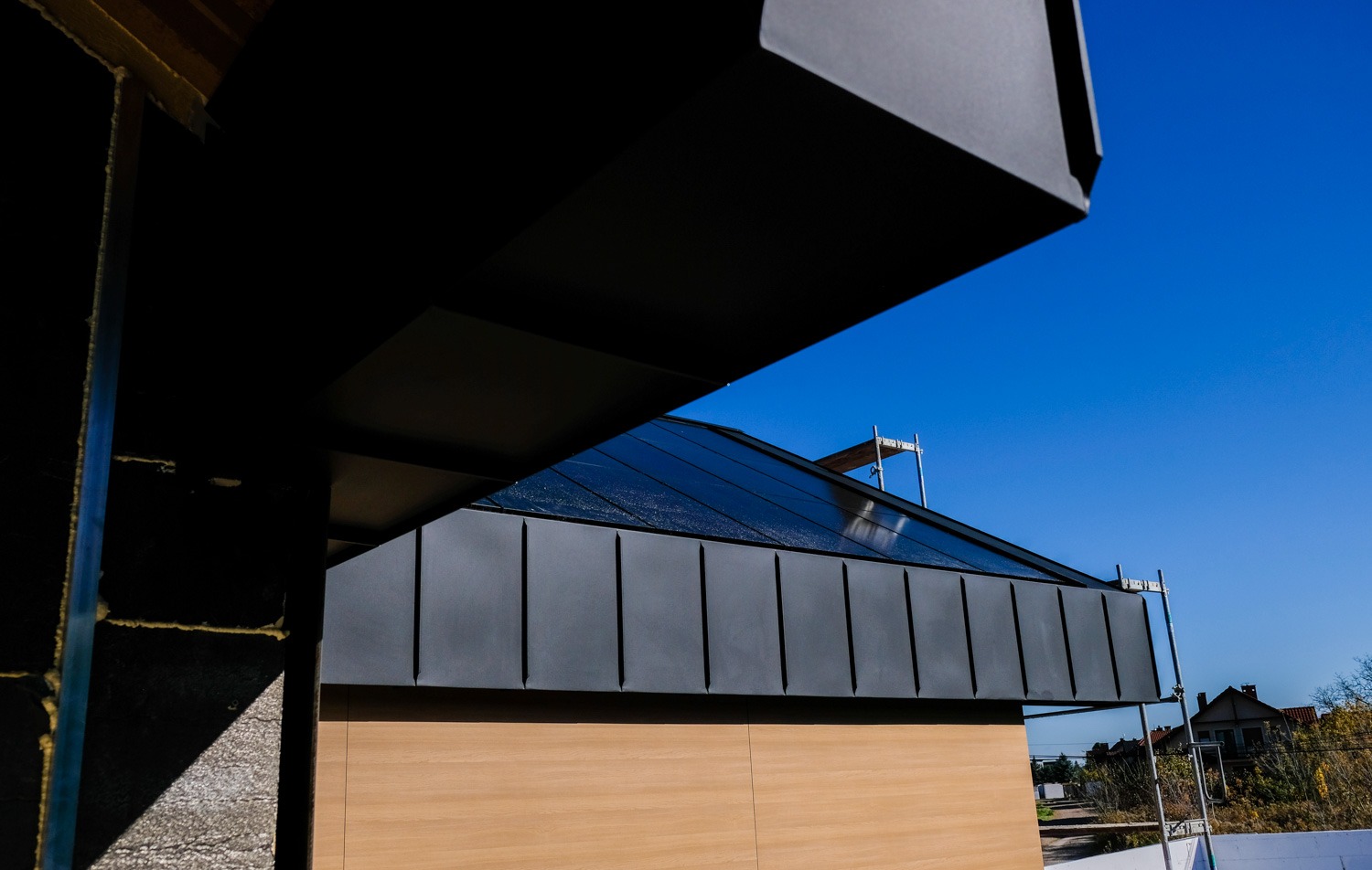 Nowoczesny dach z blachy na rąbek stojący w kolorze grafitowym, widok z dołu z elementami konstrukcji budynku w tle i rusztowaniem.