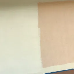 Fragment elewacji z naniesioną próbką beżowej farby obok oryginalnego kremowego koloru, zabezpieczone taśmą malarską.