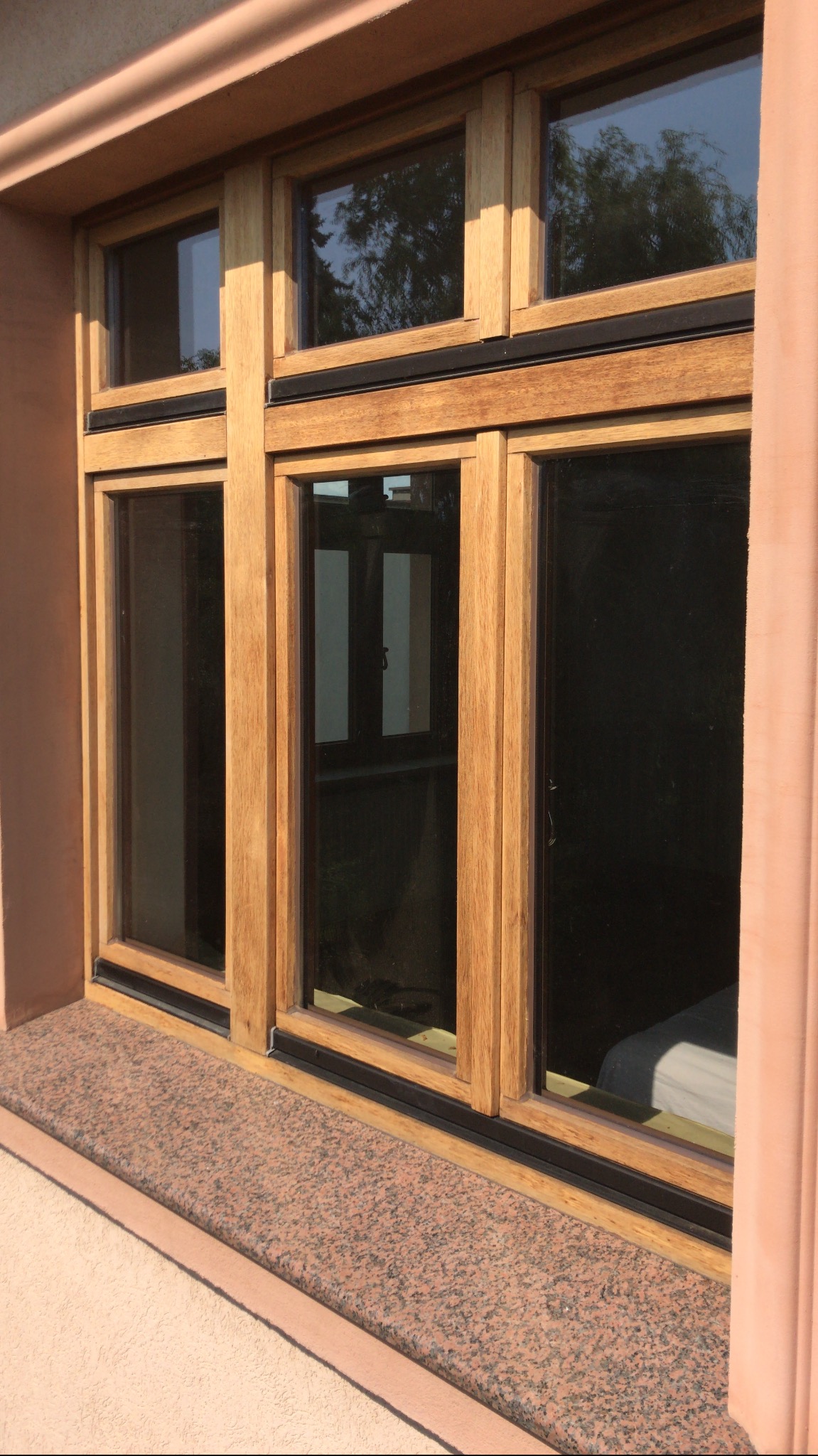 Drewniane okno z czarnymi uszczelkami w różowej elewacji, widoczny parapet z różowego granitu.