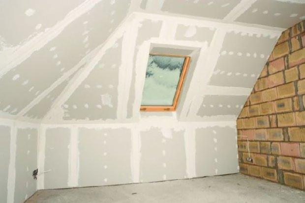 Poddasze z oknem dachowym w trakcie wykańczania: płyty gipsowo-kartonowe na ścianach i suficie, widoczna ceglana ściana szczytowa, szpachlowane łączenia płyt.