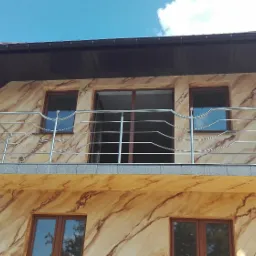 Balkon z balustradą nierdzewną na elewacji imitującej marmur, widok z dołu na tle błękitnego nieba.