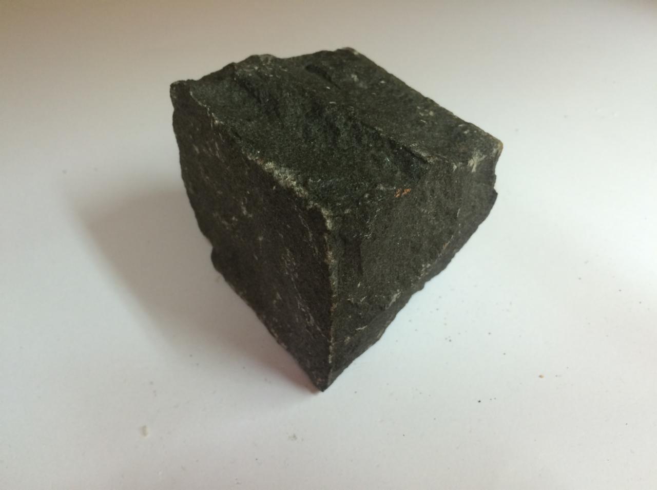 Kostka Gabro o szorstkiej powierzchni, sfotografowana na jasnym tle z widocznym cieniem, ukazująca jej teksturę i regularny kształt.