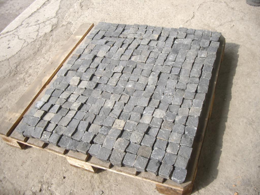 Gabro kostka ułożona regularnie na drewnianej palecie, widoczna faktura kamienia i delikatne różnice w odcieniach szarości.