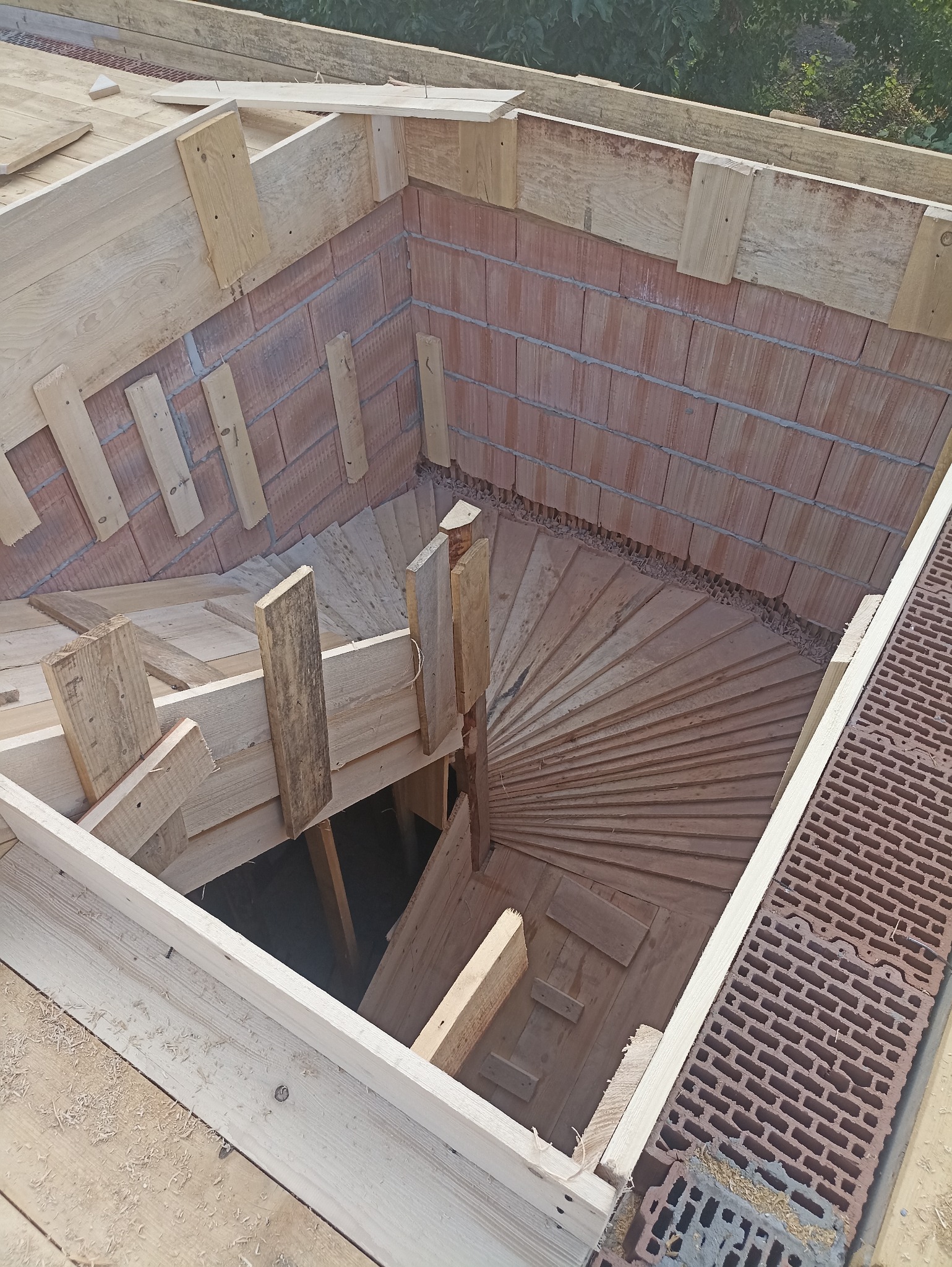 Wykonywanie schodów w otworze stropu. Widoczne drewniane szalunki, cegły i elementy konstrukcyjne. Ujęcie z góry na budowę schodów wewnątrz budynku.