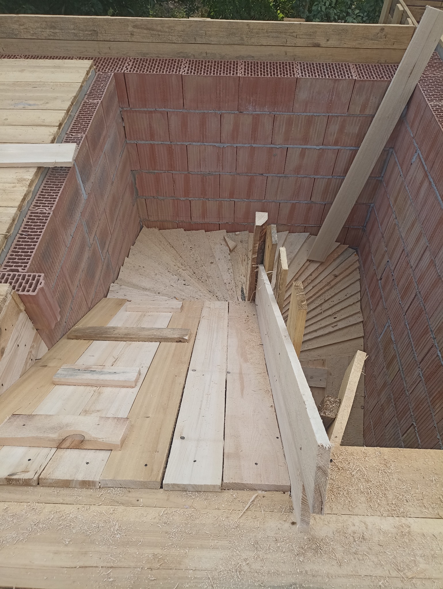 Wnętrze domu w trakcie budowy: drewniana konstrukcja stropu i fragment ściany z czerwonej cegły. Widok z góry, surowe materiały, etap budowy.