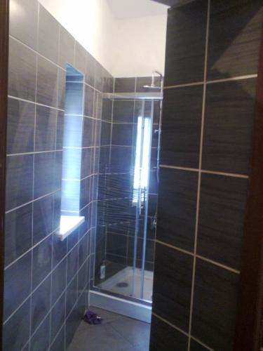 Wykończona łazienka z kabiną prysznicową i ciemnymi płytkami. Widoczna półka pod oknem i fragment drzwi. Nowoczesny design.