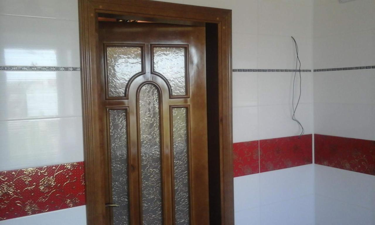 Drewniane, przeszklone drzwi wewnętrzne z dekoracyjnymi płytkami ściennymi w kolorze białym i czerwonym. Widoczne niedokończone okablowanie.