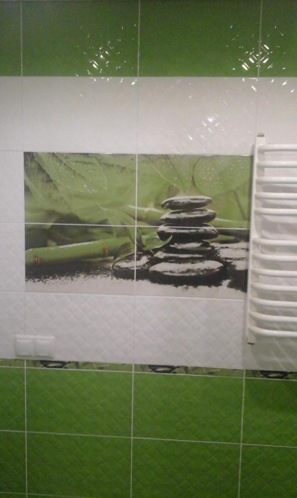 Wykończona ściana w łazience z zielono-białymi płytkami i motywem zen (kamienie i bambus) w centralnej części. Po prawej stronie widoczny biały grzejnik drabinkowy.