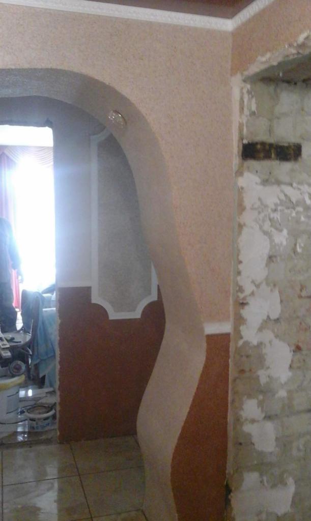 Wykończone wnętrze z łukiem i dekoracyjną strukturą na ścianie. Fragment ściany z widocznym murem, co sugeruje etap prac wykończeniowych.