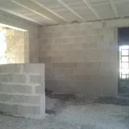 Wnętrze w trakcie budowy: ściany z bloczków, widoczne otwory okienne i drzwiowe, surowy betonowy strop. Etap wznoszenia ścian nośnych i działowych.