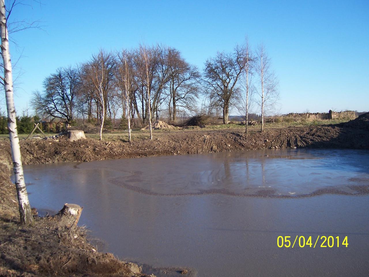 Wyrobisko ziemne wypełnione wodą, z widocznymi śladami prac ziemnych i młodymi drzewami na skraju. Data 05/04/2014 w prawym dolnym rogu.