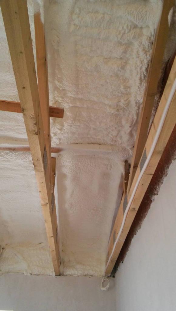 Poddasze ocieplone pianką, widoczne drewniane krokwie i warstwa izolacji, z fragmentem instalacji elektrycznej.