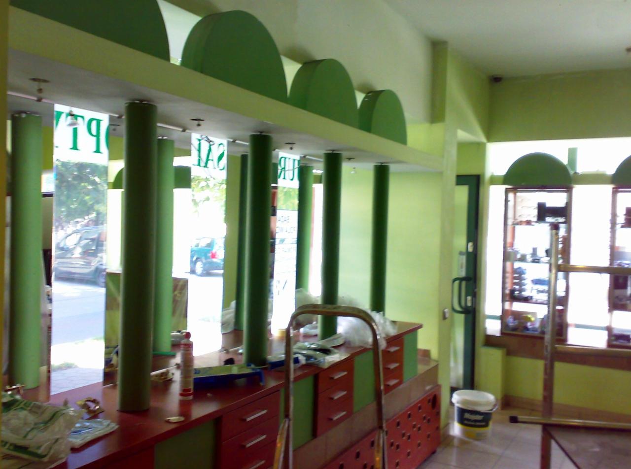 Wnętrze lokalu w trakcie odświeżania: zielone ściany, kolumny i elementy dekoracyjne, meble w kolorze czerwieni i zieleni. Widoczne narzędzia i akcesoria malarskie.