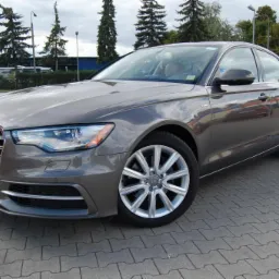 Szary Audi A6 z aluminiowymi felgami na parkingu w Człopie. Widoczne drzewa w tle. Auto zadbane, gotowe do leasingu lub kredytu.