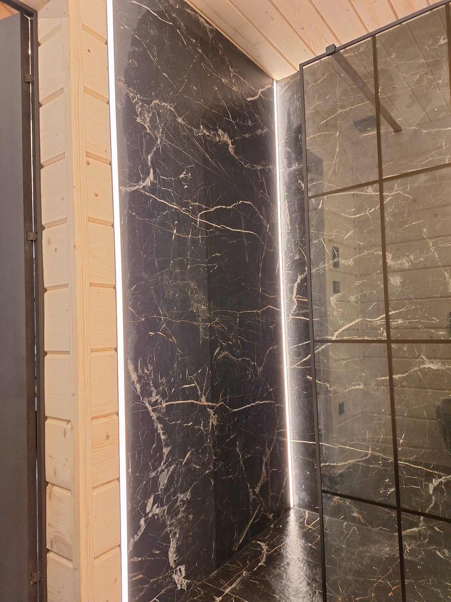 Nowoczesna łazienka z czarnymi płytami imitującymi marmur, podświetleniem LED i drewnianym wykończeniem ścian.