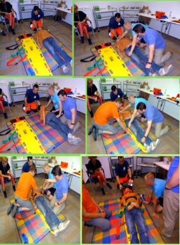 Kurs pierwszej pomocy: instruktorzy demonstrują zabezpieczanie poszkodowanego na noszach ortopedycznych. Ćwiczenia w sali szkoleniowej.