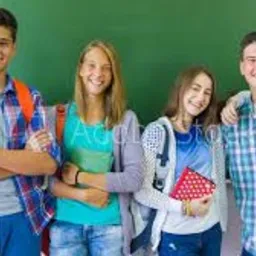 Grupa uśmiechniętych nastolatków z plecakami i książkami, stojąca na tle zielonej tablicy szkolnej.