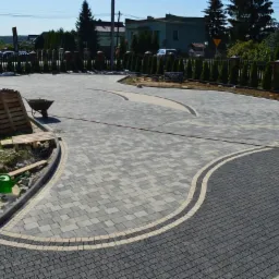 Ukończona nawierzchnia z kostki brukowej w odcieniach szarości i czerni, z paletą kostki w tle. Widoczna linia graniczna i elementy wykończeniowe.