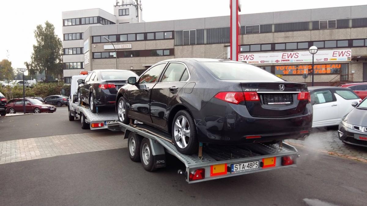 Laweta z dwoma czarnymi samochodami Honda Accord, zaparkowana przed budynkiem z szyldem 'SSS Siedle' i 'EWS'. Widoczna tablica rejestracyjna STA 48P5.