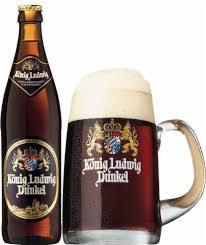 Butelka i kufel ciemnego piwa König Ludwig Dunkel na białym tle. Kufel wypełniony po brzegi pianą, etykieta butelki z herbem. Idealne na imprezę.