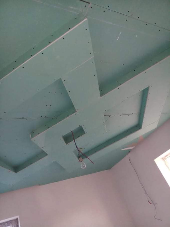 Sufit z płyt kartonowo-gipsowych z dekoracyjnymi wgłębieniami w kształcie krzyża, widoczne ślady po wkrętach, wystające kable i żarówka, ściany pomalowane na jasny kolor.