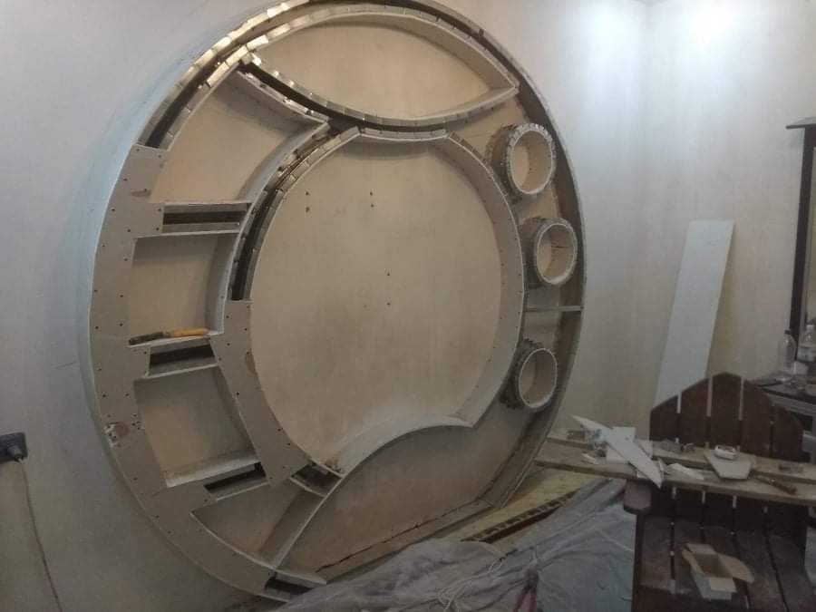 Niezwykła okrągła konstrukcja z płyty kartonowo-gipsowej z wnękami i półkami, widoczna w trakcie montażu, z widocznymi śladami po szpachlowaniu i elementami mocującymi.