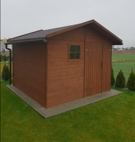 Gotowa, brązowa, drewniana konstrukcja z oknem i dwuskrzydłowymi drzwiami, stojąca na trawniku z kostką wokół.