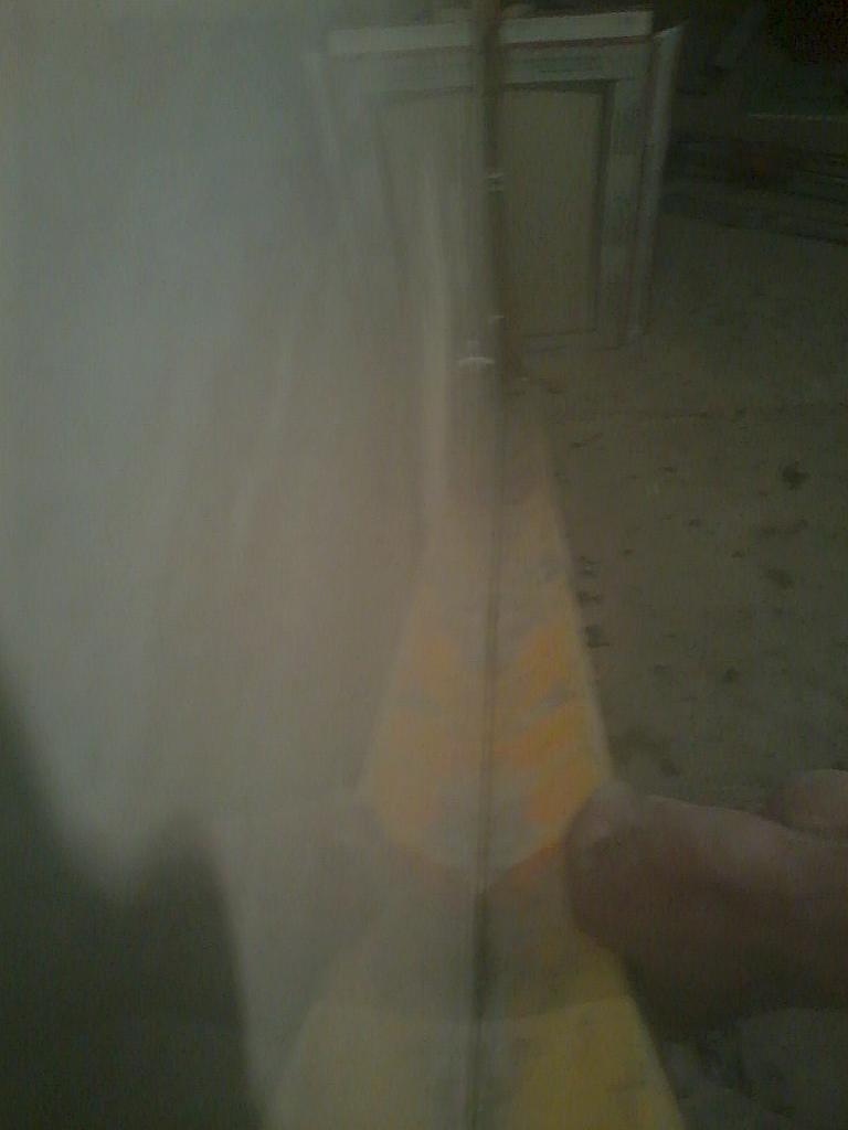 Świeżo pomalowana ściana w pomieszczeniu, widoczna mokra powierzchnia i fragment dłoni. Ujęcie z bliska, słabe oświetlenie.