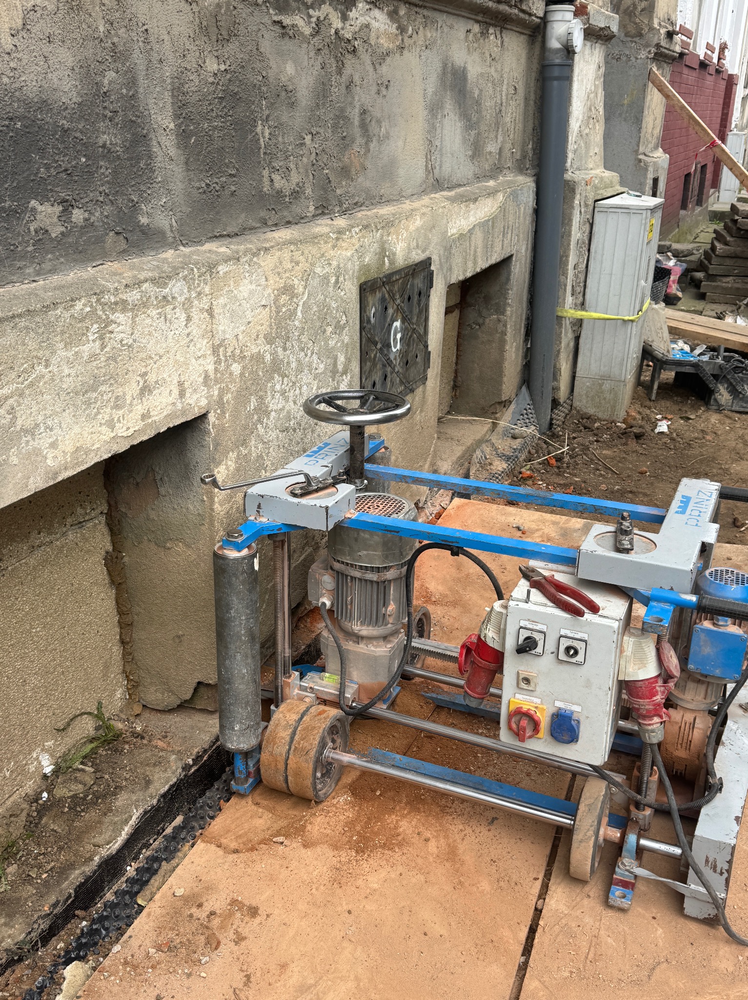 Specjalistyczna maszyna do cięcia betonu przy fundamencie starego budynku. Widoczna szczelina w fundamencie, przygotowana pod hydroizolację. Narzędzia pracy na maszynie.