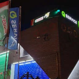 Oświetlony budynek warsztatu samochodowego nocą z logo firmy i flagami reklamowymi.