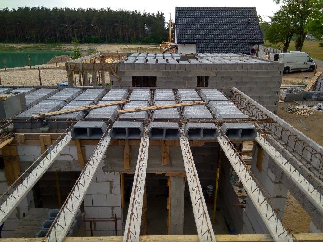 Budowa domu: widok z góry na strop Teriva z pustakami betonowymi, zbrojenie wieńca, ściany z bloczków, w tle jezioro i las.