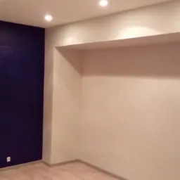 Pomalowane na granatowo ściana w nowo wykończonym pokoju z jasnymi ścianami, drewnianą podłogą i wnęką w ścianie pod sufitem.