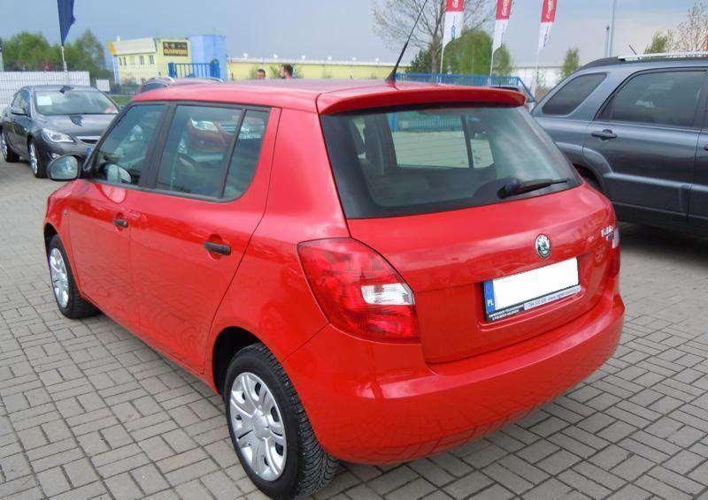 Czerwona Skoda Fabia z widocznym tylnym światłem, spoilerem i tablicą rejestracyjną na tle kostki brukowej i innych aut. Ujęcie z boku i tyłu.