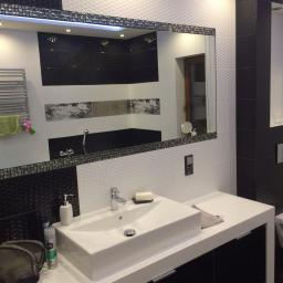 Usługi Remontowo-Budowlane - Nowoczesna łazienka z białą umywalką nablatową, czarno-białymi płytkami z fakturą i lustrem w ozdobnej ramie, odbijającym wnętrze łazienki z czarną wanną.