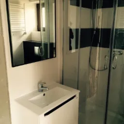 Nowoczesna łazienka z kabiną prysznicową z zaokrąglonymi drzwiami i białą szafką pod umywalką z czarnym akcentem, widok w lustrze na grzejnik drabinkowy i czarną szafkę.