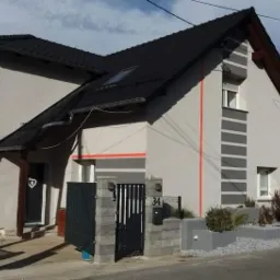 Dom jednorodzinny w Gostomii po odnowieniu elewacji z szarymi pasami i pomarańczowymi akcentami, widok z zewnątrz na ogrodzenie i wejście.