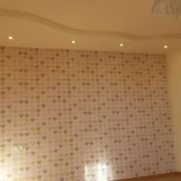 Pokój po remoncie: ściana w tapetę w serduszka, podwieszany sufit z oświetleniem punktowym, fragment drabiny malarskiej. Nowoczesne wykończenie wnętrz.