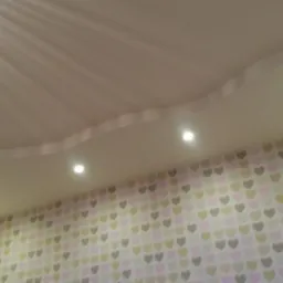 Dekoracyjny sufit podwieszany z oświetleniem punktowym nad ścianą w tapetę w serduszka. Falista linia sufitu dodaje wnętrzu unikalnego charakteru.