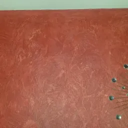 Czerwona ściana z dekoracyjnym wzorem, uzupełniona o nowoczesny zegar z metalowymi promieniami i kryształkami, dodający wnętrzu charakteru.