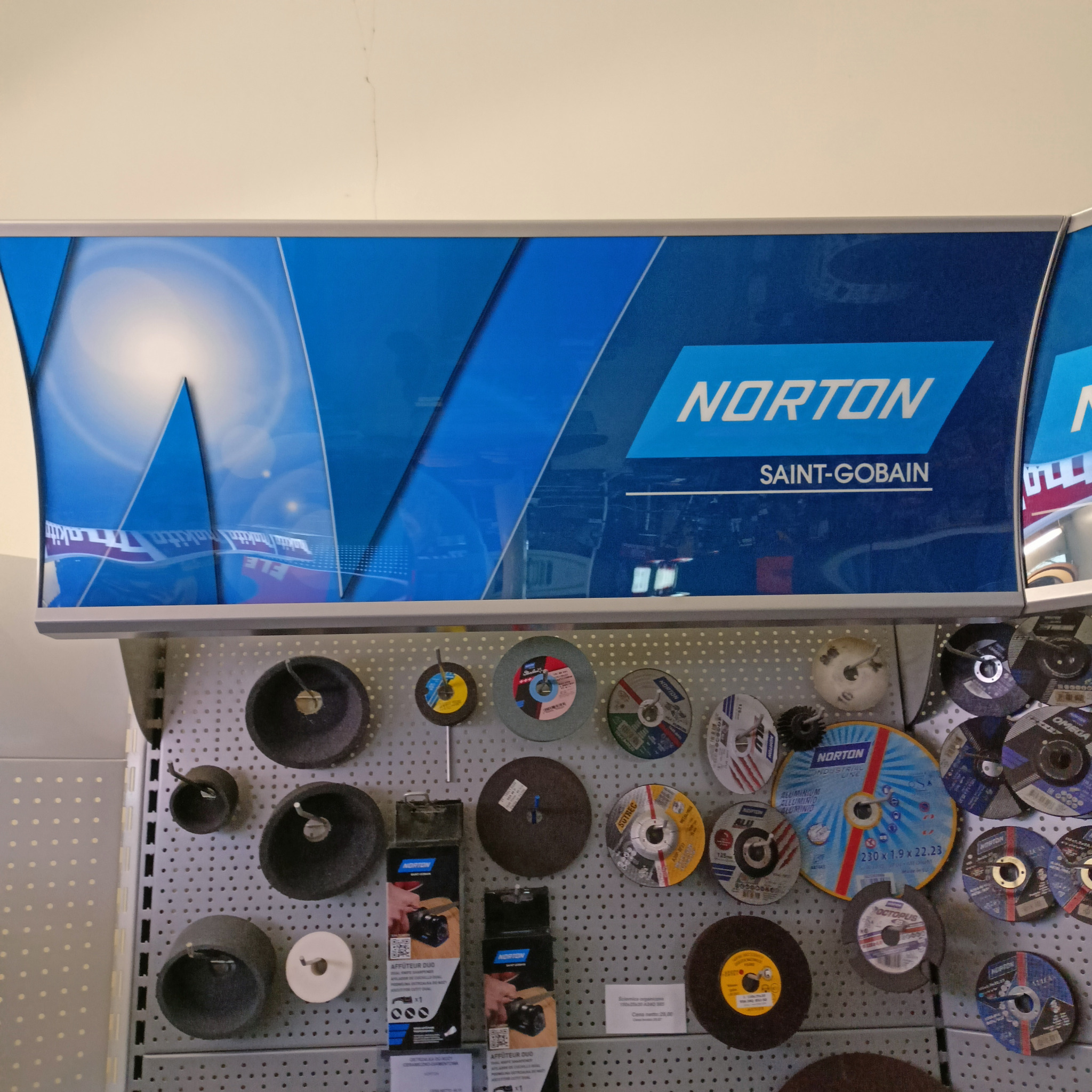 Ekspozycja różnych tarcz szlifierskich i ściernic marki Norton na perforowanej ścianie w sklepie.