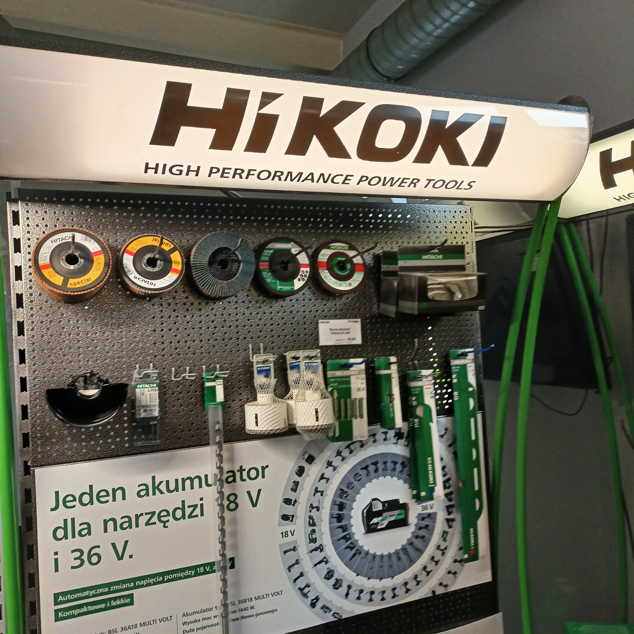 Ekspozycja materiałów eksploatacyjnych i akcesoriów marki HiKOKI do elektronarzędzi, w tym tarcze szlifierskie, wiertła i akumulatory Multi Volt, prezentowane na perforowanej ścianie ekspozycyjnej...